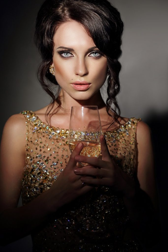 a gorgeous high-class woman holding a drink, looking at the camera
