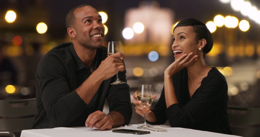 Charming black male tells his lovely date something funny while drinking wine