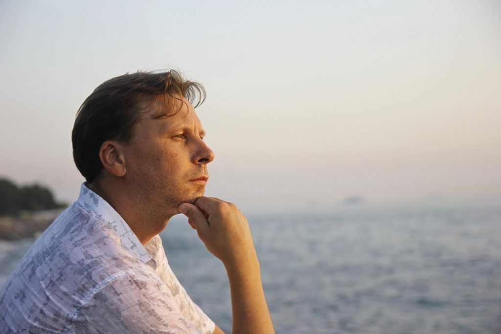 man sitting near water engaging in active retrospection trying to figure out how to become a fun person