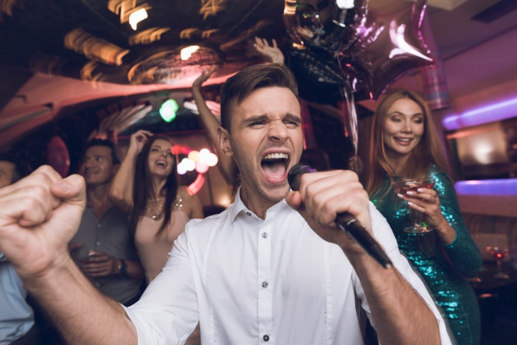 man in white shirt singing in nightclub having a great time with girls who are enjoying his company