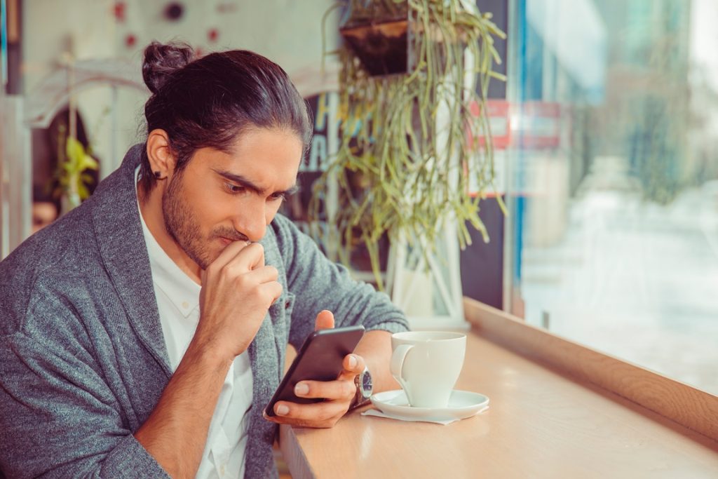 man looking at his phone with anxiety because a girl takes forever to respond but seems interested
