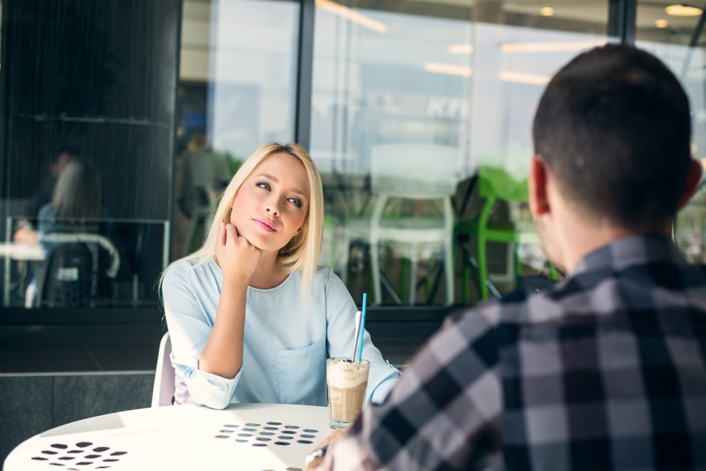 young guy and girl are on a long first date sitting at a cafe, girl is looking at him and listening intently